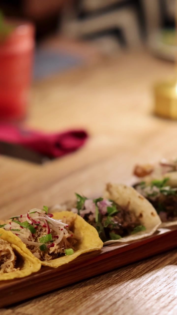 Nærbillede af tacos på et træfad i en varmt oplyst restaurantindstilling, der fremhæver levende ingredienser og indbydende atmosfære