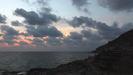 Eine-Landschaftsaufnahme-Eines-Atemberaubenden-Roten-Sonnenuntergangs-In-Thailand-Mit-Einem-Dramatischen-Himmel-Mit-Dunklen-Wolken,-Die-Den-Himmel-Bedecken,-Und-Sonne,-Die-Durch-Die-Wolken-über-Dem-Friedlichen-Ozean-Scheint