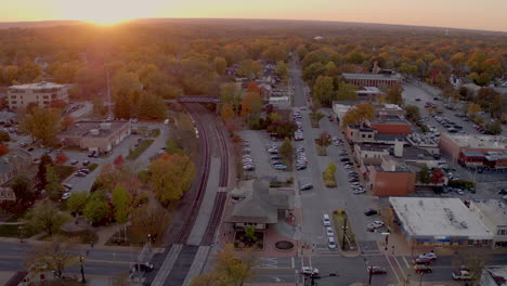 aerial push over train tracks and train station and main street of charming small town in autumn at sunset on a beautiful evening, clip one of two continuous clips