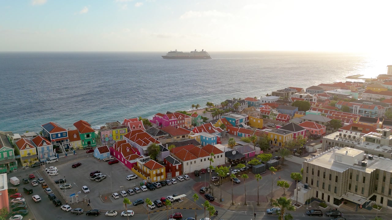Aerial sunset reveal of Pietermaai with colorful waterfront buildings and warm light across Willemstad coastline.