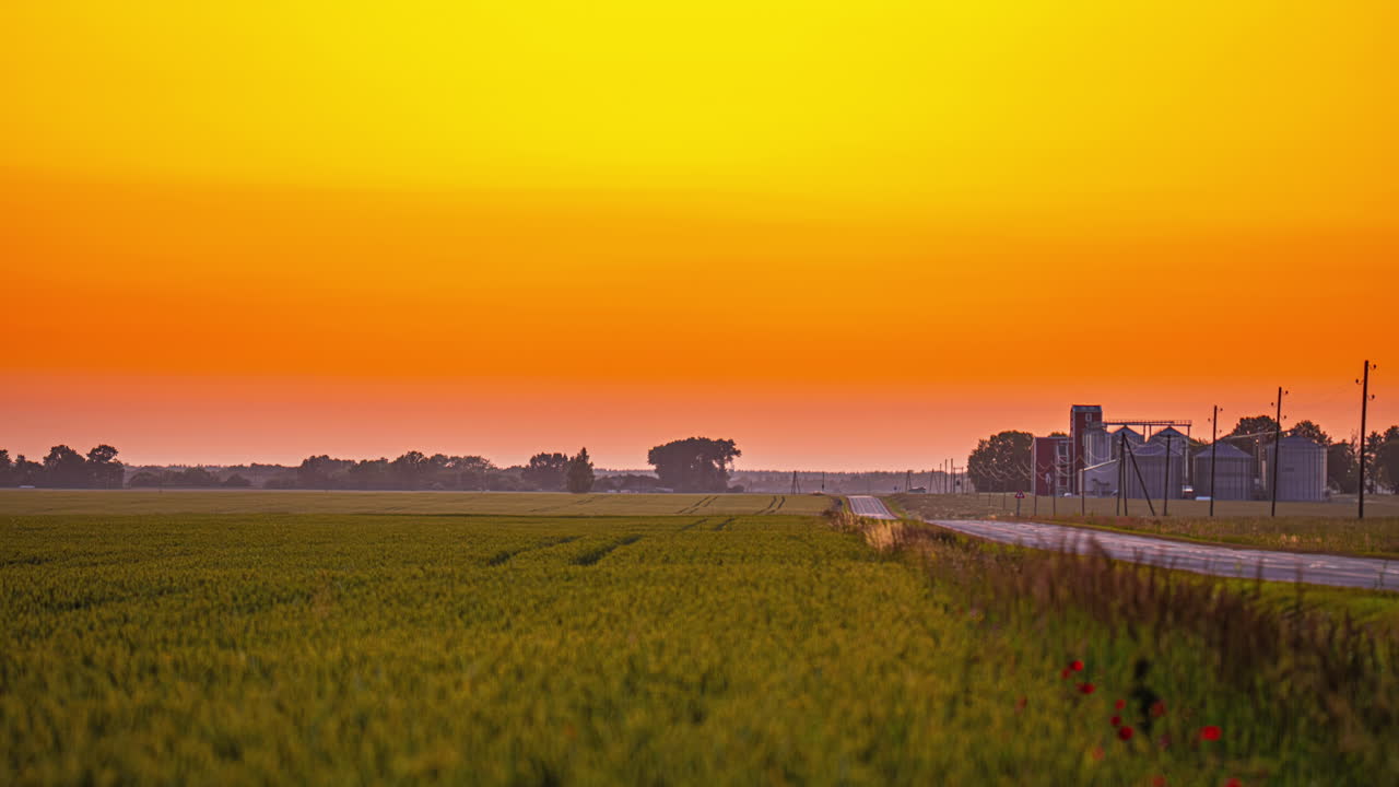 과 멀리 있는 곡물 엘리베이터가 있는 평온한 시골에 황금빛 해가 지는 모습