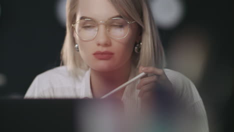 gedachtevolle zakenvrouw op zoek naar laptop in een donker kantoor. vrouw die op de werkplek werkt