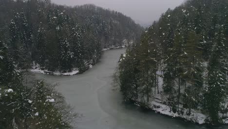 Aerial-shot-of-frozen-lake-surrounded-by-forest-at-winter