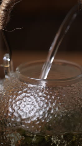 pouring hot water into glass teapot with green tea leaves