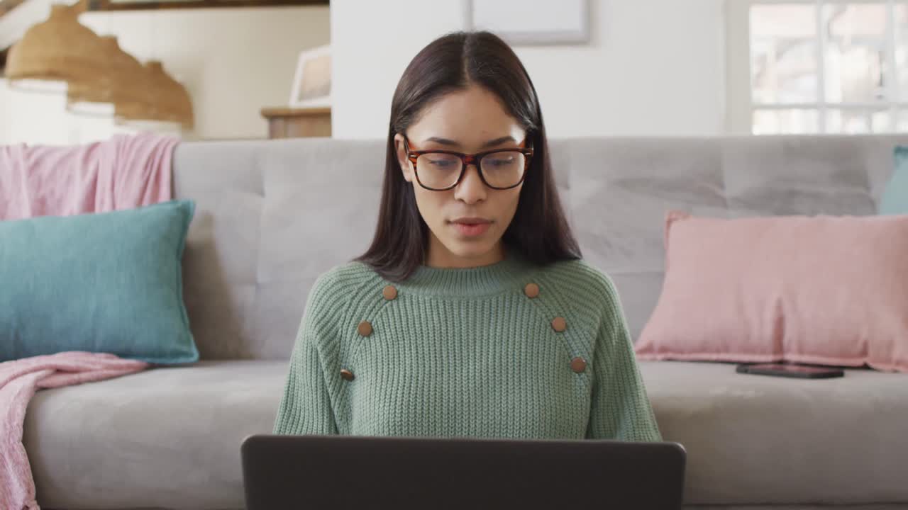 mujer biracial usando una computadora portátil y trabajando en la sala de estar