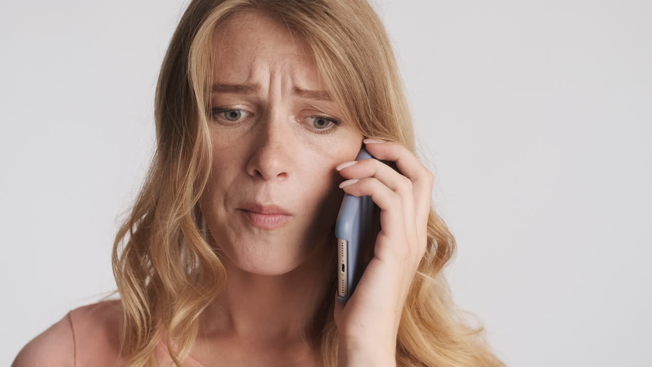 Caucasian woman chewing a gum while talking on the phone on camera.