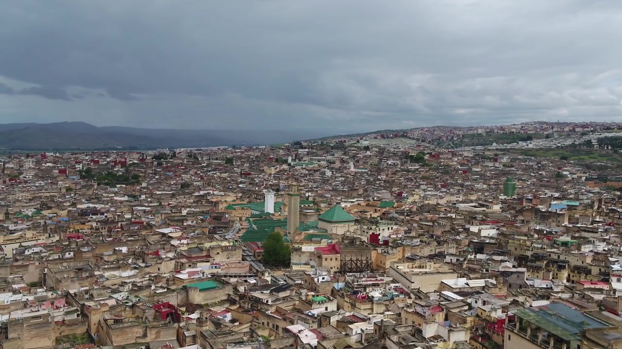 Fas'taki yeşil tepelerin ve yoğun tarihi Fes Medine'sinin, dramatik bulutlu gökyüzü altında geniş açılı havadan drone görüntüsü, seyahat ve belgesel projeleri için ideal.