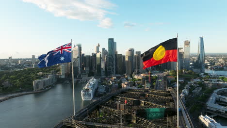 flag of australia and aboriginal flag on top of sydney harbour bridge with panoramic view of cbd skyline in sydney, australia