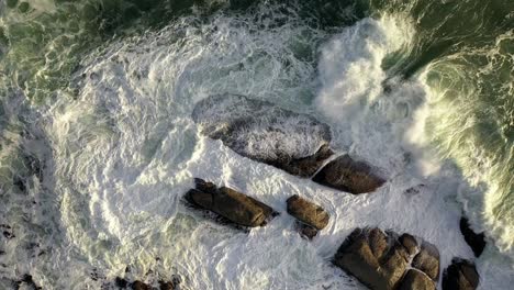 mezmerizing cinematic cenital suave ascenso tiro de ásperas olas del océano golpeando rocas durante la puesta de sol en la playa de la bahía de campamentos de ciudad del cabo