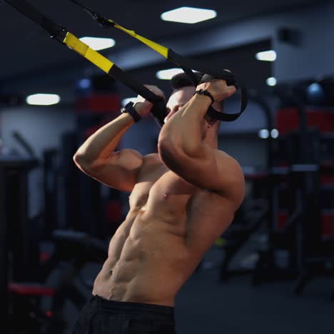 sportive guy in the gym. muscular man without shirt pumping muscles on a simulator with a rubber at sports centre. daily workout of bodybuilder