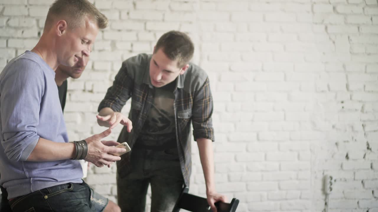 3명의 남성 동료들이 커피 휴식시간에 사무실에 앉아 스마트폰에 앱을 사용하고 있다.