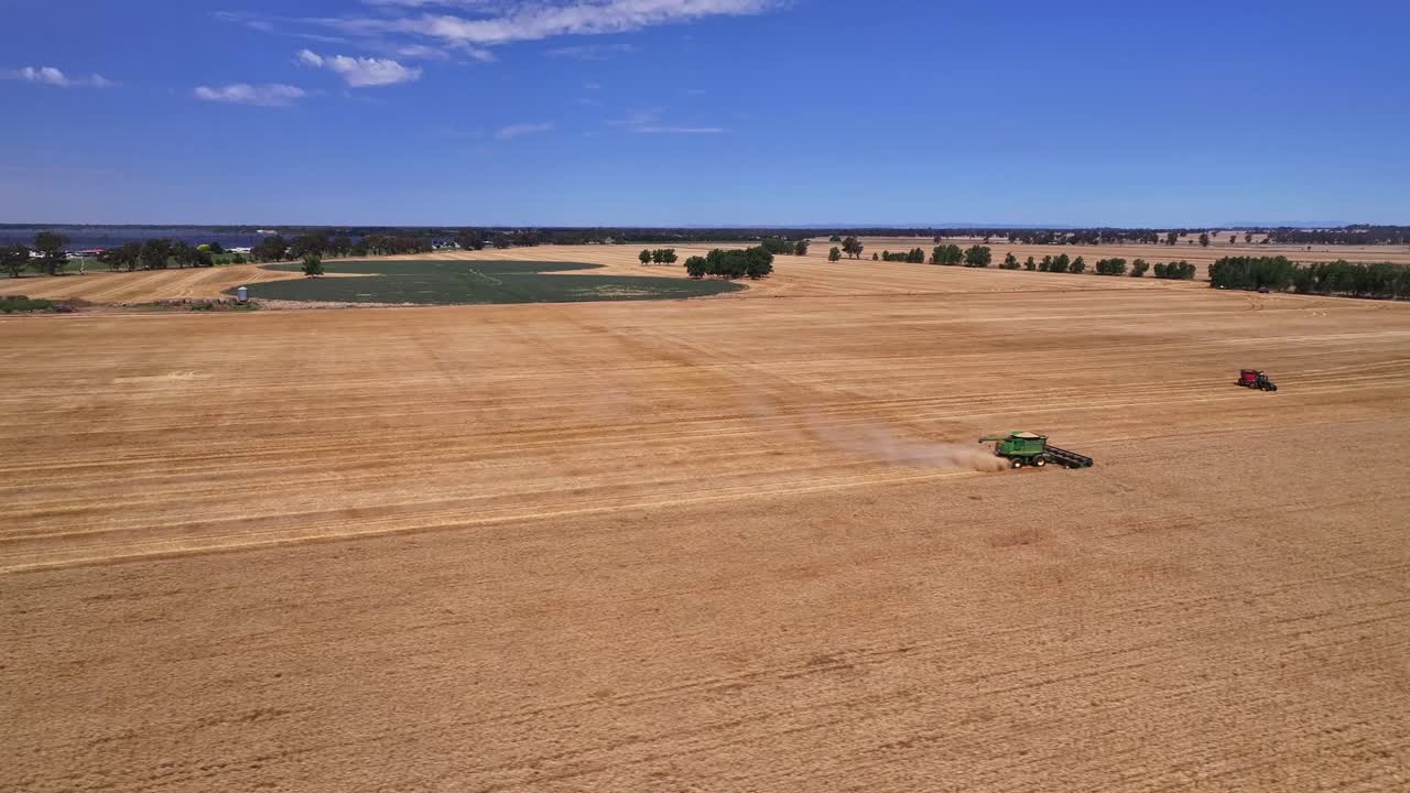 High shot of a harvester working in a paddock with Lake Mulwala and paddocks beyond