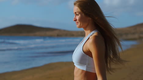 a woman in sports clothes comes to the ocean and looks into the distance touching her hair. slow motion steadicam