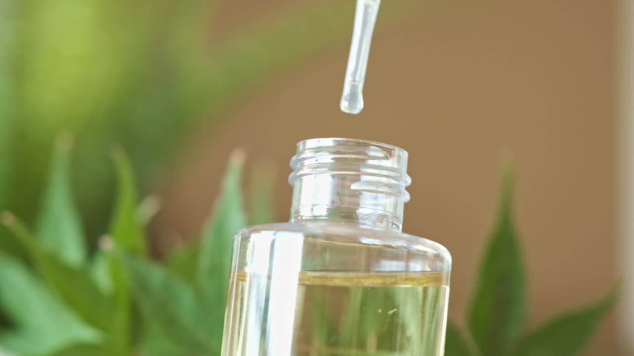 aceite de cbd en cámara lenta, cayendo en una botella de vidrio transparente con hojas de marihuana en segundo plano