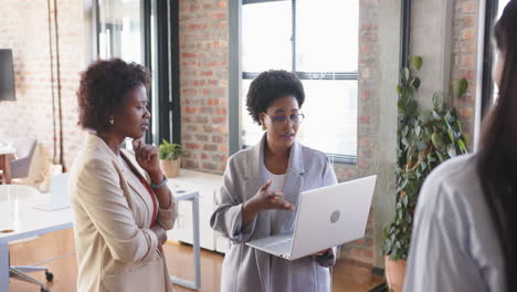 using laptop, businesswomen discussing project in modern office space