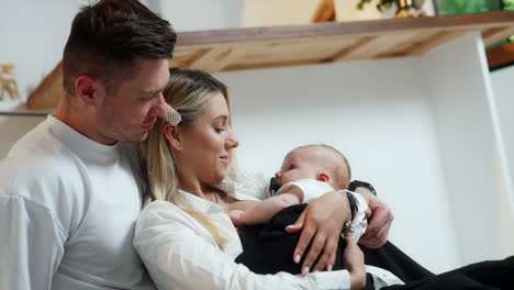 woman holding a baby leaned on her husband standing behind. happy parents looking at their child.