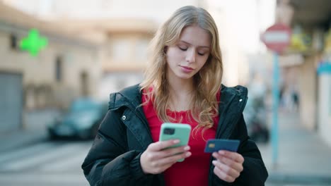 young blonde girl using smartphone and credit card at street