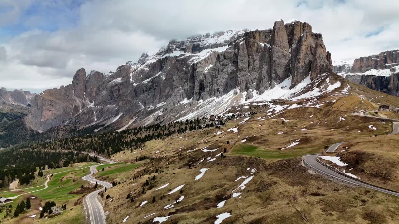 A stunning aerial view of Sella Pass in the Dolomites, Italy, where a winding alpine road cuts through dramatic snow-capped peaks