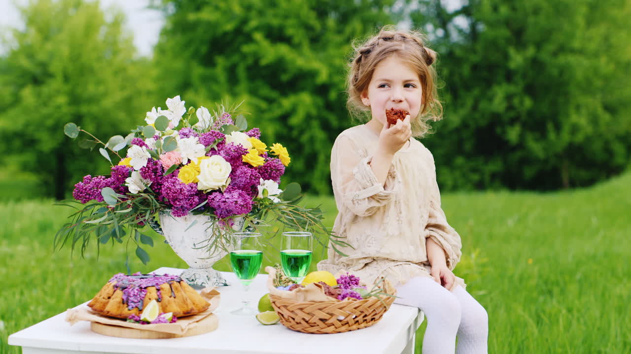 linda niñita con un vestido elegante y brillante se sienta en una mesa y come manos con dulces de chocolate