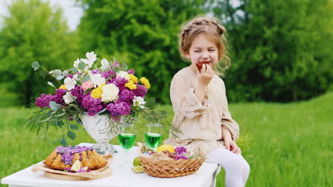 cute little girl in a bright smart dress sits on a table and eats hands with chocolate sweets