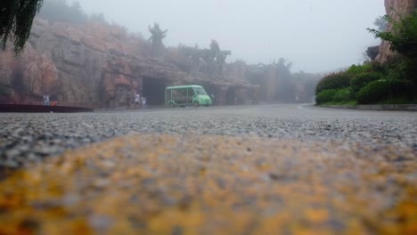 Toma-De-ángulo-Bajo-De-Un-Vehículo-De-Autocar-Verde-En-La-Niebla-O-Lluvia-Ligera-Frente-A-Un-Clima-Tormentoso-Y-Turistas-Que-Viajan-En-Un-Día-Lluvioso