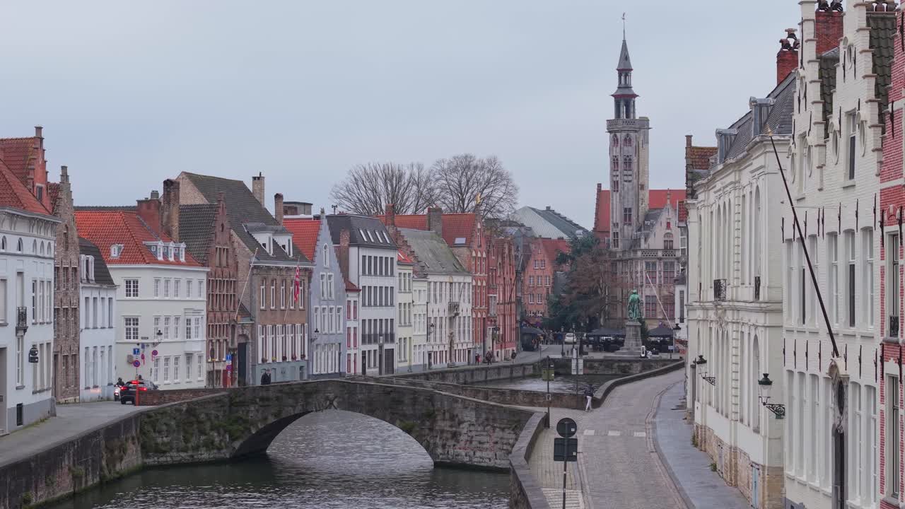 Aerial reveal shot over King's Bridge (Koningsbrug) in Bruges, showing traditional waterside houses and the iconic Jan Van Eyck sculpture in the background. Historic Flemish architecture in Belgium