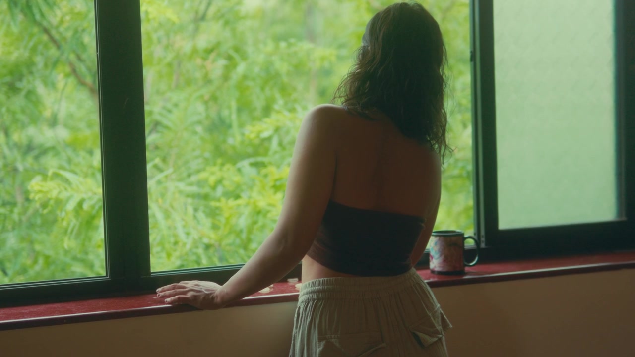 Woman standing by window with coffee looking at lush greenery outside in peaceful indoor setting