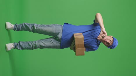 full body of unsatisfied asian male courier in blue uniform showing thumbs down gesture while delivering a carton on green screen background in the studio