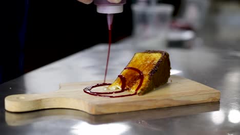 pouring raspberry sauce to a slice of creme brulee cheesecake - ready for serving - close up