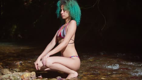 a woman in a bikini squats at the river edge on a tropical island in the caribbean