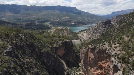 Vista-Aérea-Colinas-Y-Montañas-Con-Un-Bosque-Al-Lado-Del-Lago,-El-Paisaje-Natural-Bajo-Un-Cielo-Nublado,-Presa-Construida-En-El-Cañón