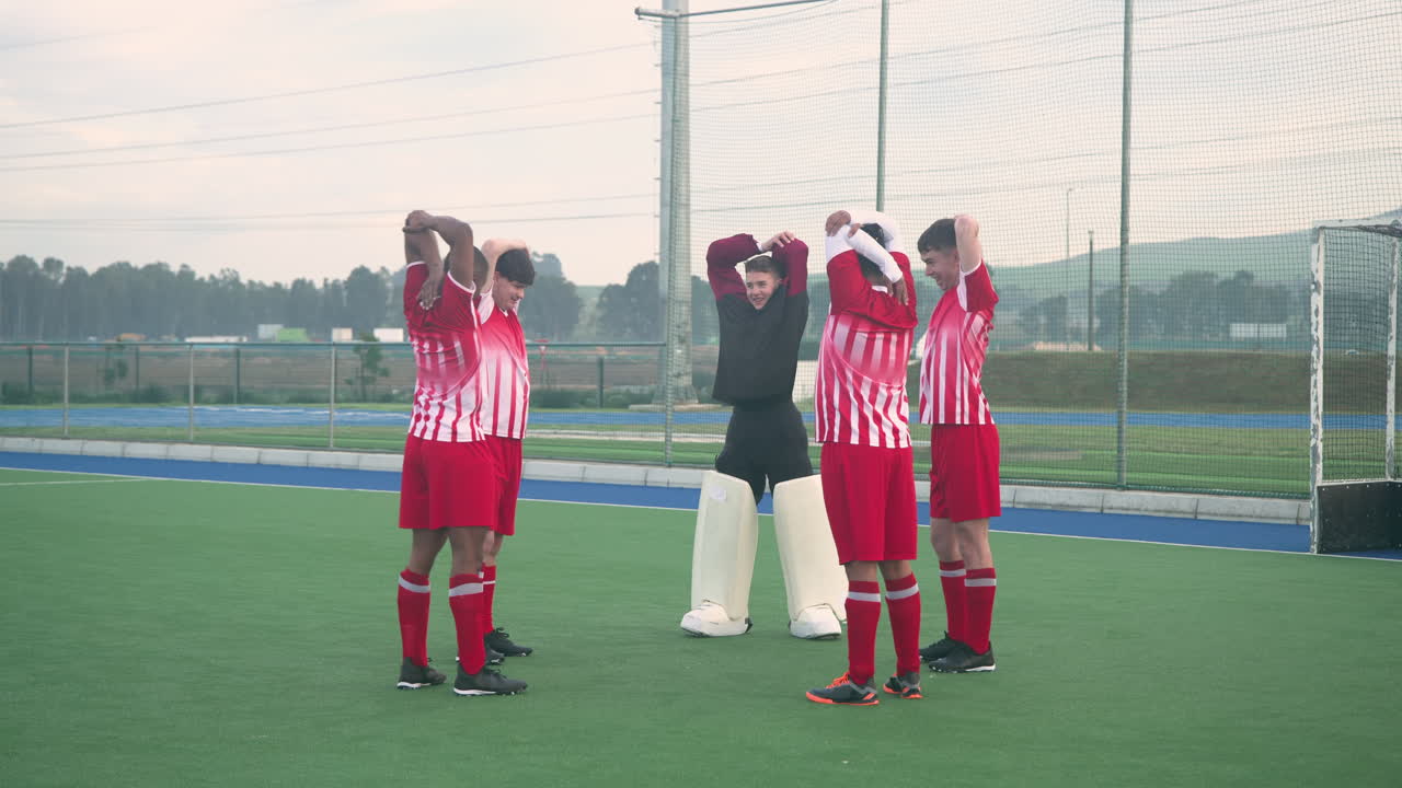 Hockey players in red uniforms stretching with goalkeeper on field before game