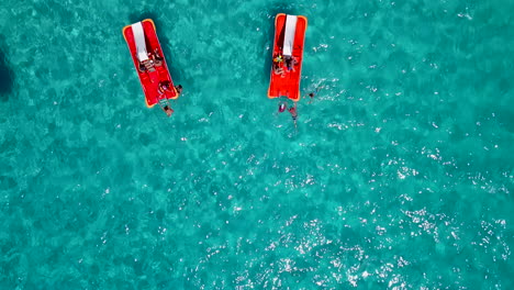 Aerial-shot-of-two-red-pedal-boats-in-shallow-crystal-clear-blue-waters-at-a-holiday-resort