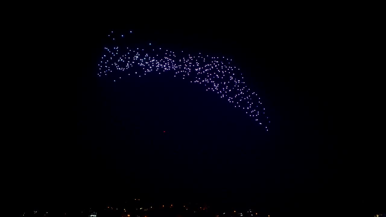 도시 상공을 비행하는 밤하늘에 추상 모델을 만드는 밝은 조명을 가진 드론