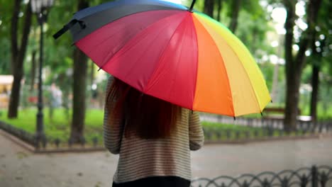 Rückansicht-Einer-Nicht-Wiederzuerkennenden-Frau,-Die-Mit-Buntem-Regenschirm-Unter-Dem-Regen-Im-Stadtpark-Läuft.-Zeitlupenaufnahme