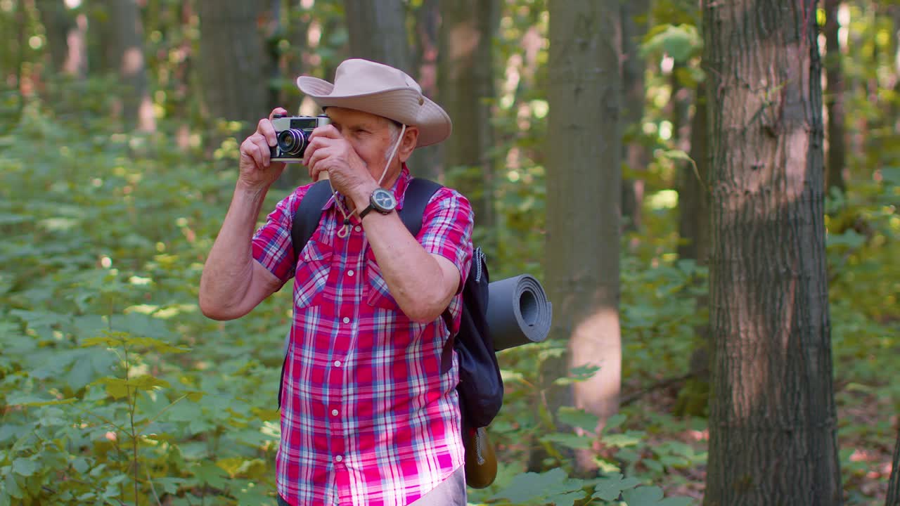 hombre mayor abuelo en un viaje de senderismo explorando la vida silvestre tomando fotos en el bosque con cámara retro