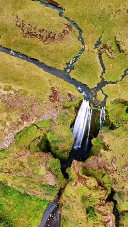 jaw-dropping crack in the ground with a waterfall falling to the bottom. breath-taking view of the mountain in iceland. a group of tourists stands at the cave. top view. vertical video.