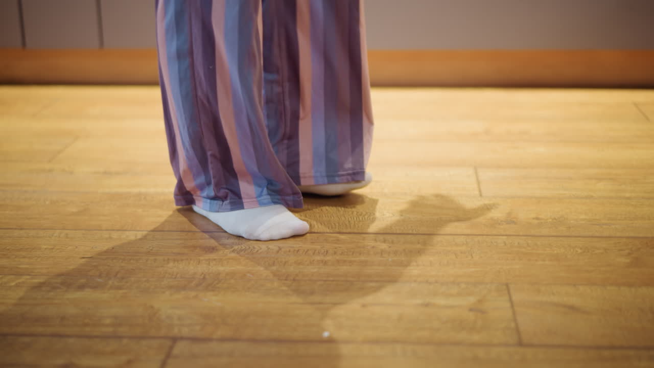 Closeup of person standing on wooden floor wearing white socks and striped loose pants with purple and pink tones, casual indoor outfit showing cozy lifestyle, comfort, and everyday home atmosphere