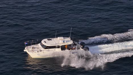 aerial tracking shot of a commercial fishing charter boat speeding across open ocean waters near port douglas, australia, in warm sunset lighting