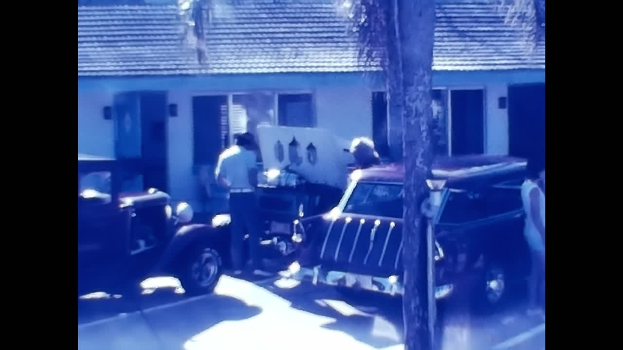 Man Standing Next to Car in Front of House at Old Car Show in 1970s USA. CIRCA USA - 1970s: A man stands next to a car parked in front of a house at an old car show in the 1970s in the United States.