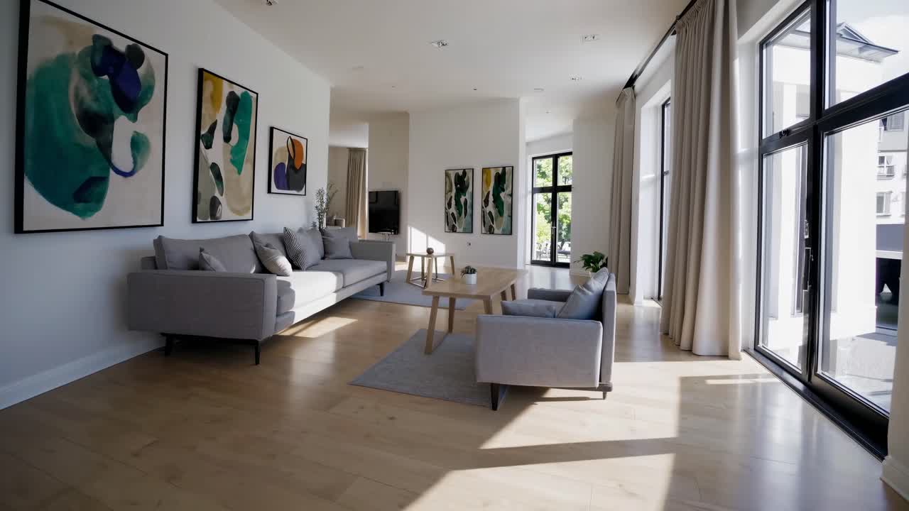 Wide-angle video shot of a modern living room with abstract art, neutral tones, and large windows