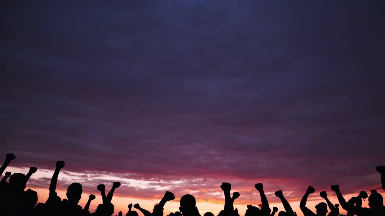 Silhouetted crowd with raised fists against a vibrant sunset sky, captured from a low angle
