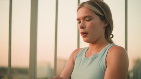 young lady sitting near iron railing cleaning dirt from palm, taking deep breath while gazing into distance with peaceful expression, evening sunlight illuminating her face