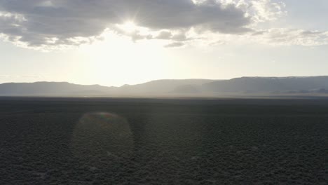 expansive desert landscape with distant mountains and sunburst at sunrise or sunset