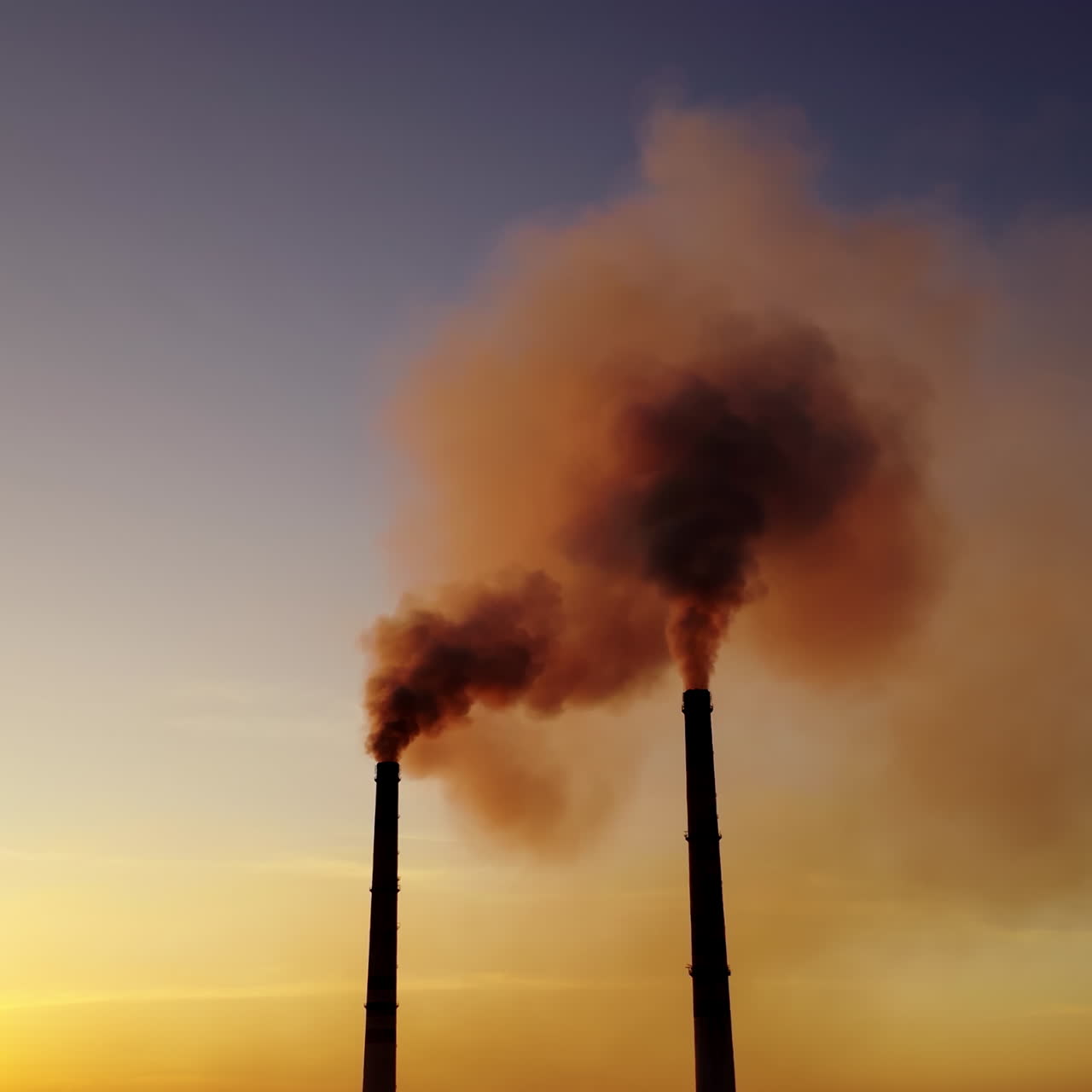Orange smoke from pipes at sunset. Dirty emissions in the air on the evening sky background. Ecology pollution.