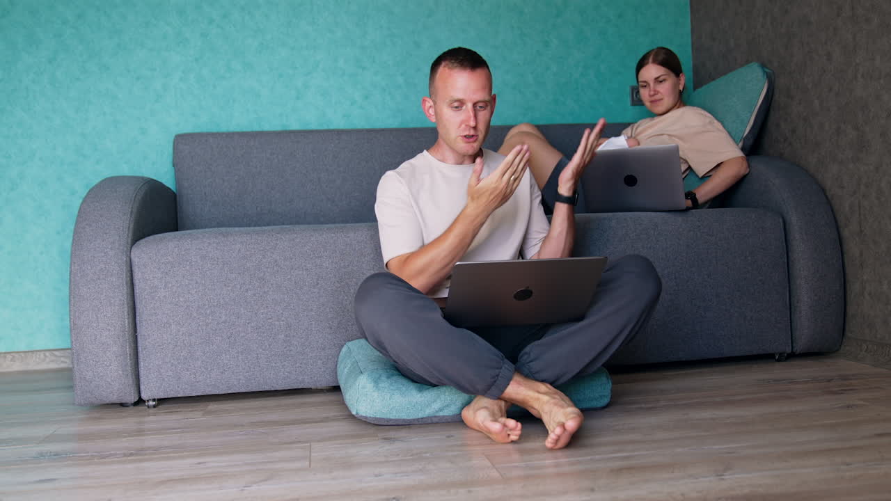 Caucasian married couple working remote at home. Parents of a newborn work on their laptops. Mother holding a baby.