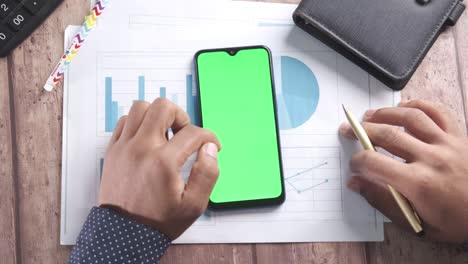 person reviewing business documents and charts with a smartphone displaying a green screen