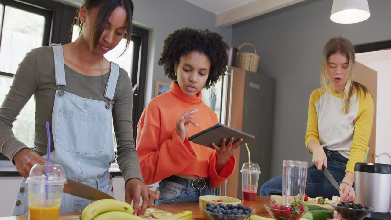 diversas amigas adolescentes cortando frutas y usando tableta en la cocina, cámara lenta