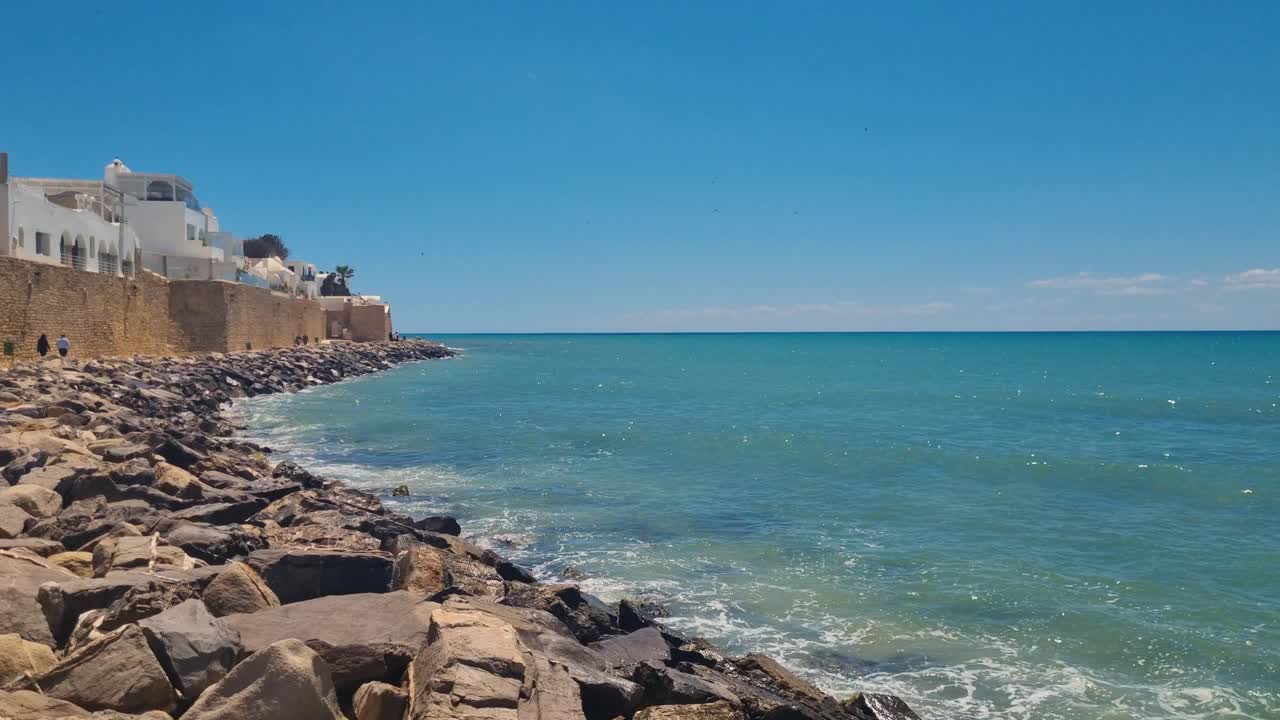 Picturesque rocky coastline in Hammamet, Tunisia, with traditional white houses overlooking turquoise Mediterranean waters on a sunny day, coastal architecture, clear sea, and holiday atmosphere