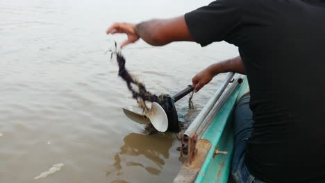 unrecognizable man unravel trash from screw propeller on tonle sap lake cambodia